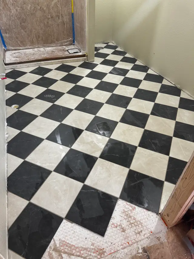 Bathroom mid-install with black and white checkerboard tile being laid