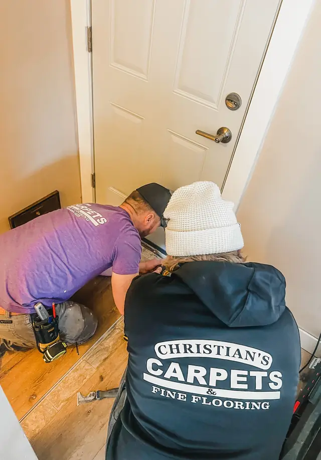 Two Christian's Carpets installers fitting flooring at a doorway, one in a company jacket